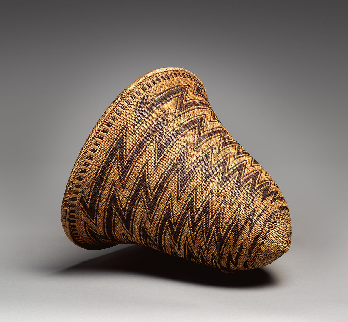 A photograph of a wicker basket made of tree shoots, woven with a zig zag pattern. 