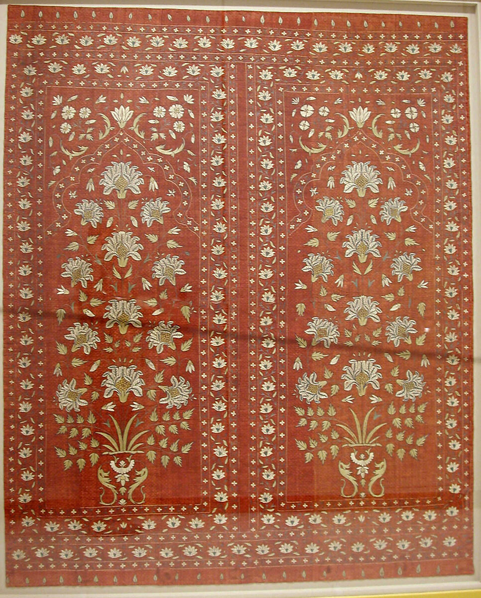 A red peice of fabric is decorated with white flowers in intricate patterns. 